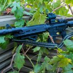 Two point paracord gun sling on a rifle. Primary color woodland camo. Secondary color black. Double cobra weave.