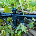 Two point paracord gun sling on a rifle. Primary color woodland camo. Secondary color black. Double cobra weave.